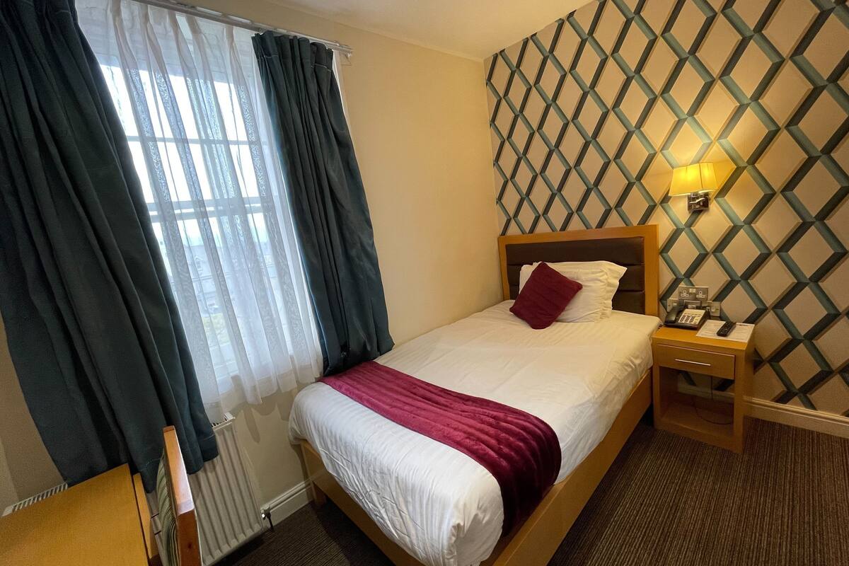 A hotel room with a bed, a nightstand, a lamp, and a patterned wall.