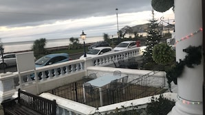 Ein Balkon mit Sitzgelegenheit im Freien, Blick auf das Meer und geparkte Autos.