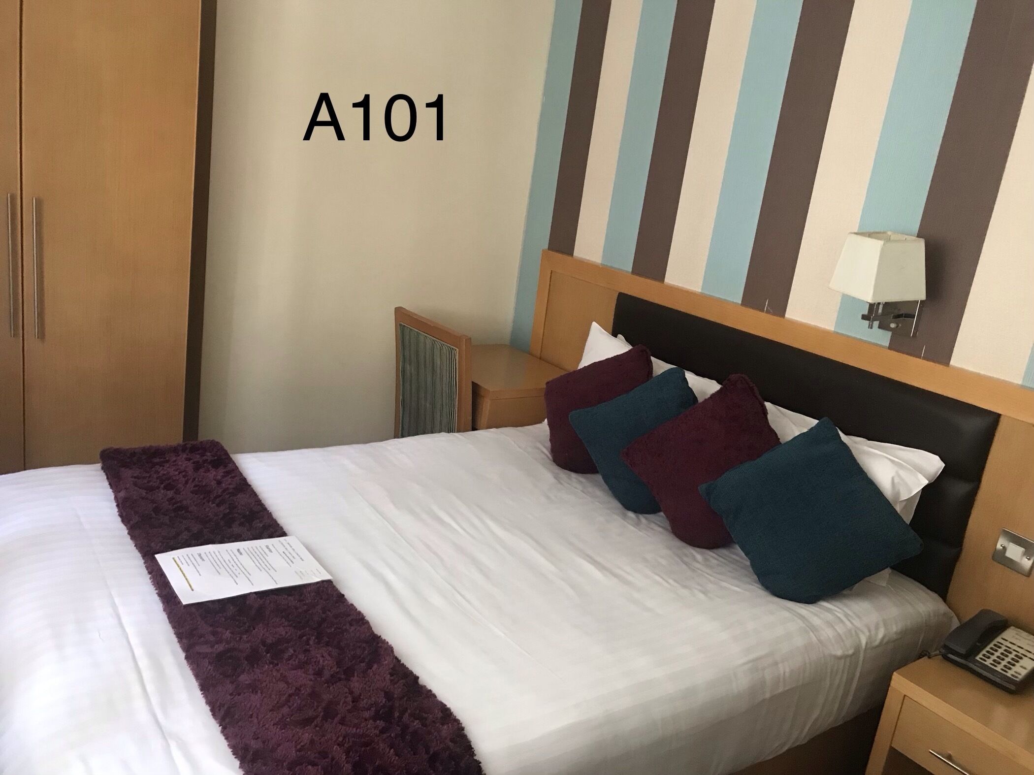 Une chambre d’hôtel avec un lit, une table de chevet, une lampe et une armoire.