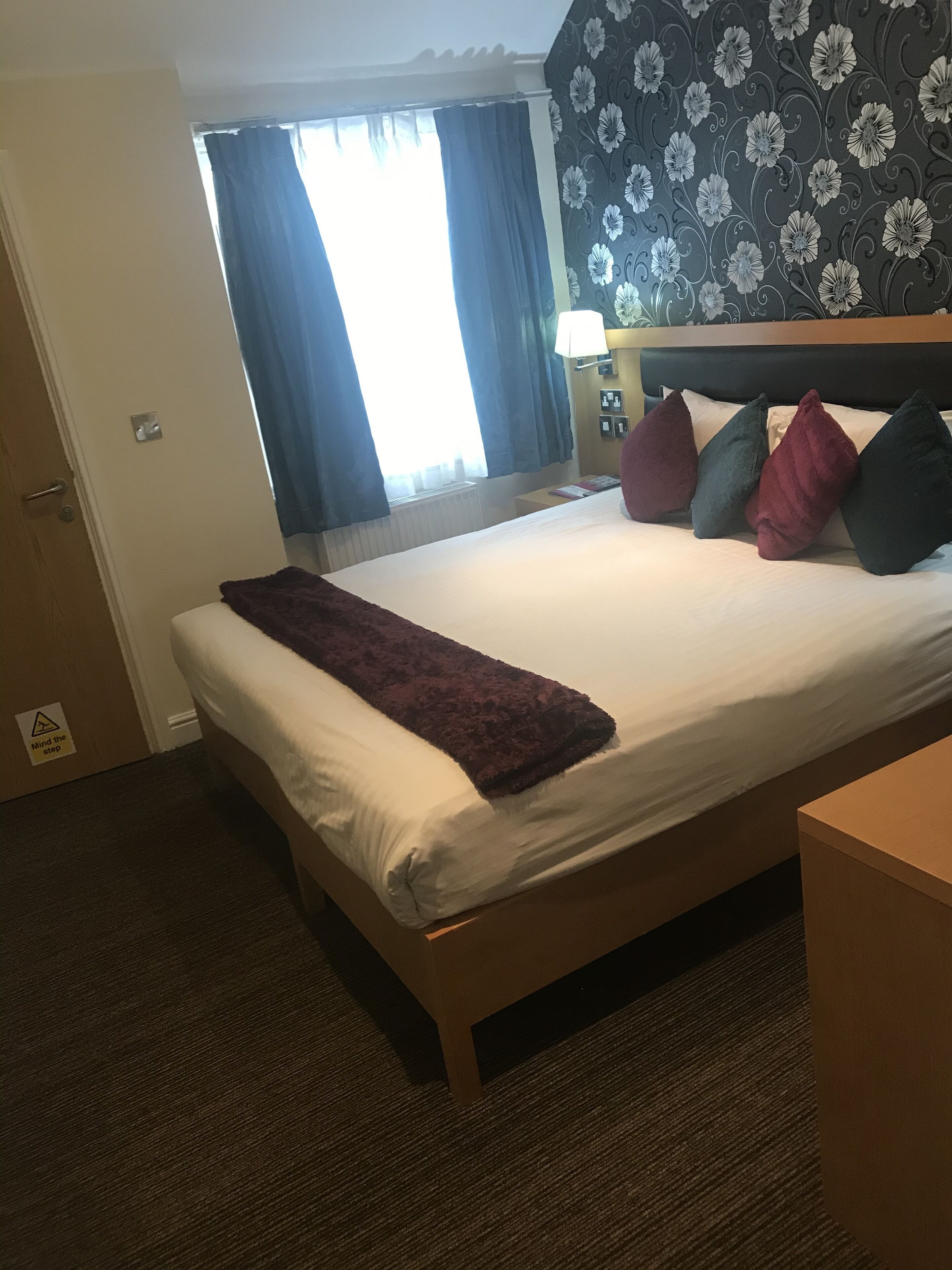 Una habitación de hotel con una cama, una mesita de noche, una lámpara y una ventana con cortinas.