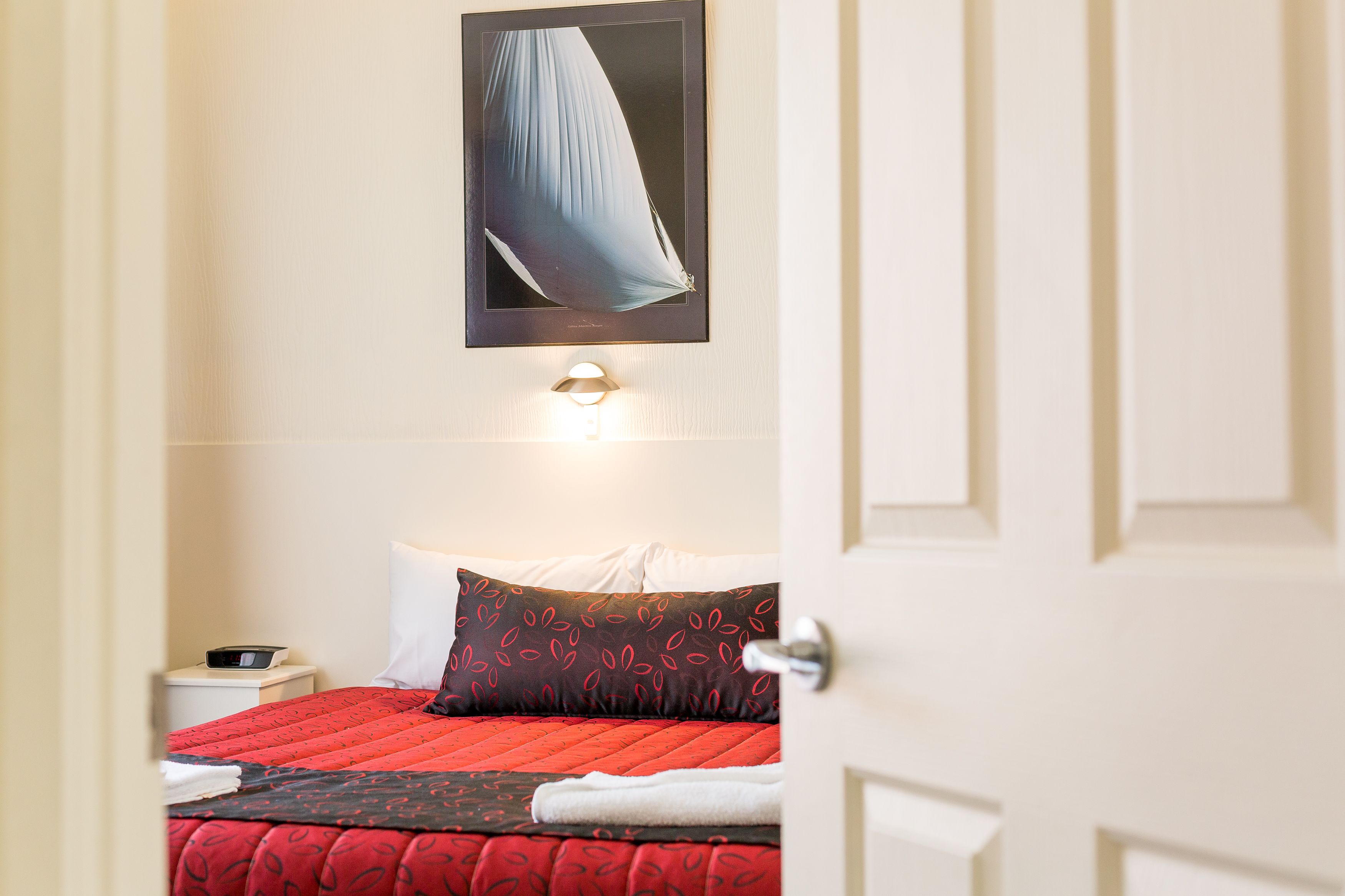 Quarto de hotel com cama, mesa de cabeceira, obra de arte na parede e uma porta.