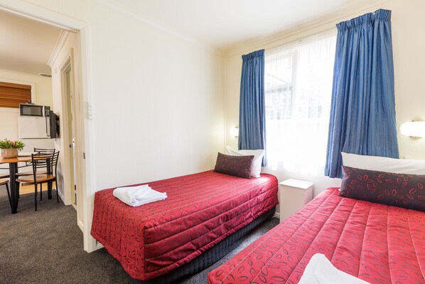 A hotel room with two beds, a desk with a chair, a microwave, and a small table with a plant.