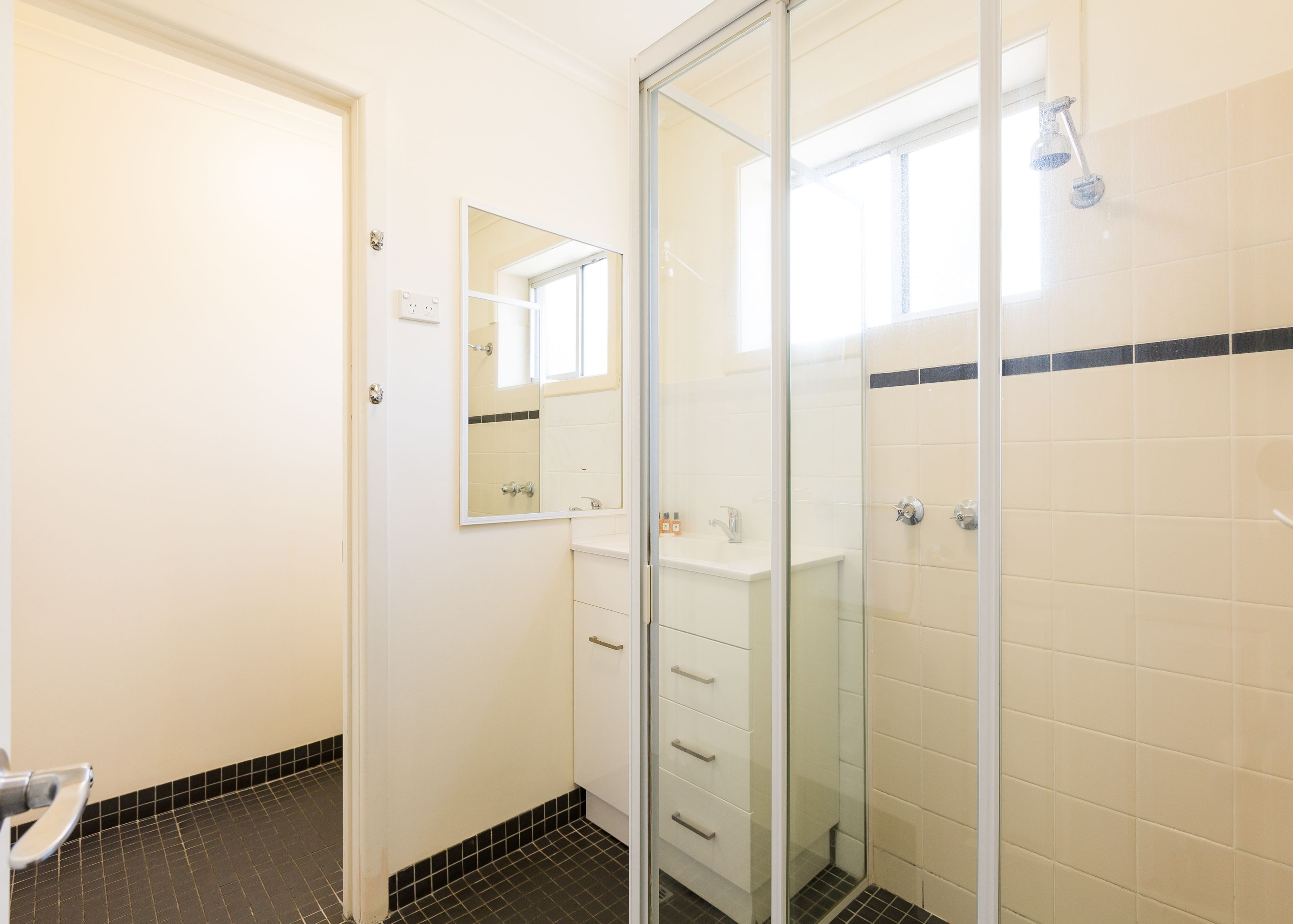 Un bany amb plat de dutxa de vidre, un lavabo blanc i un mirall.