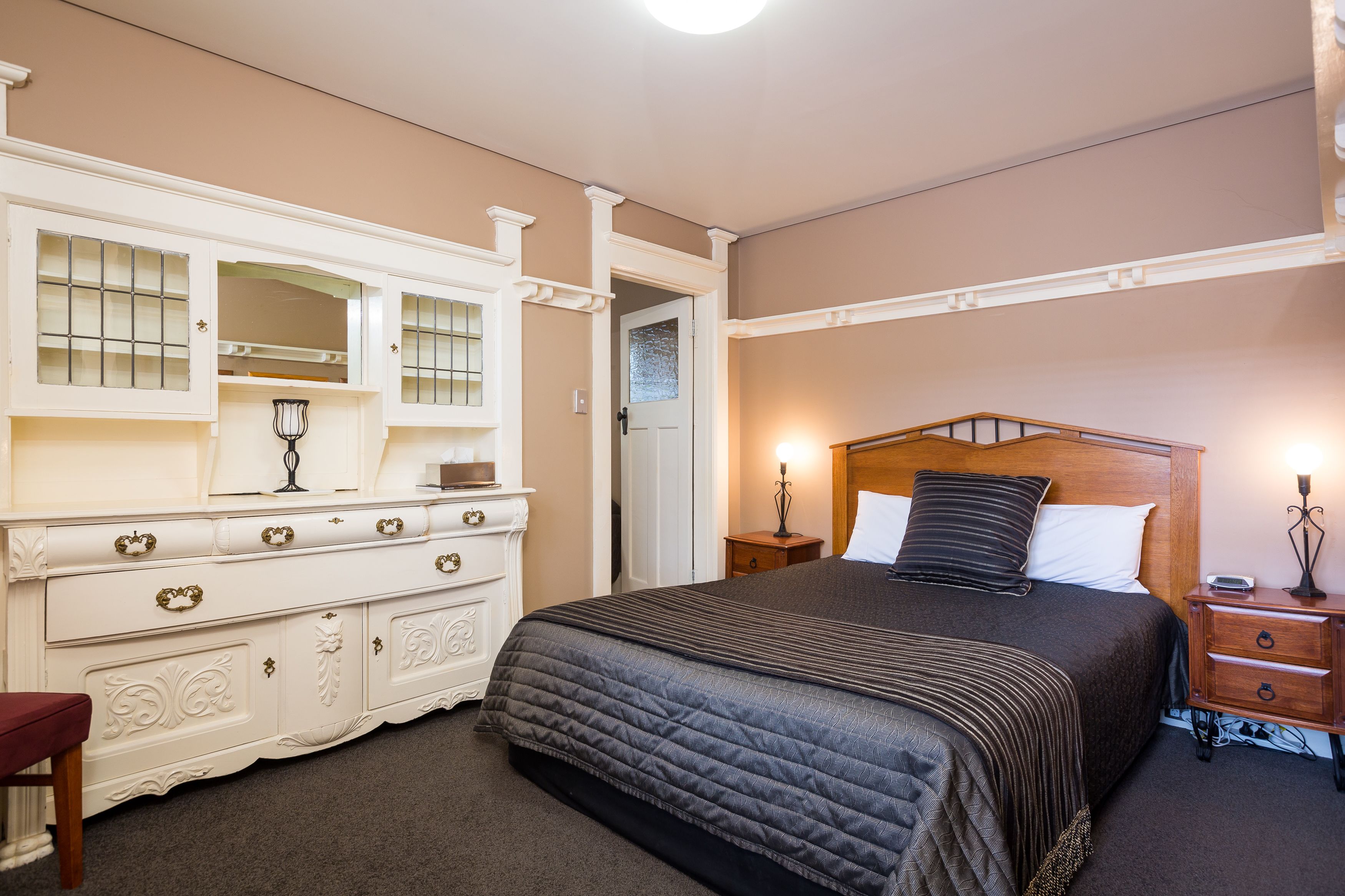 Een slaapkamer met een groot bed, een dressoir met meerdere lades, een nachtkastje en een spiegel boven het dressoir.