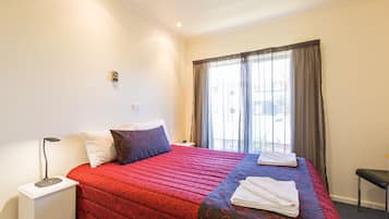 A hotel room with a bed, a bedside table, a lamp, a window with curtains, and a view of the outside.