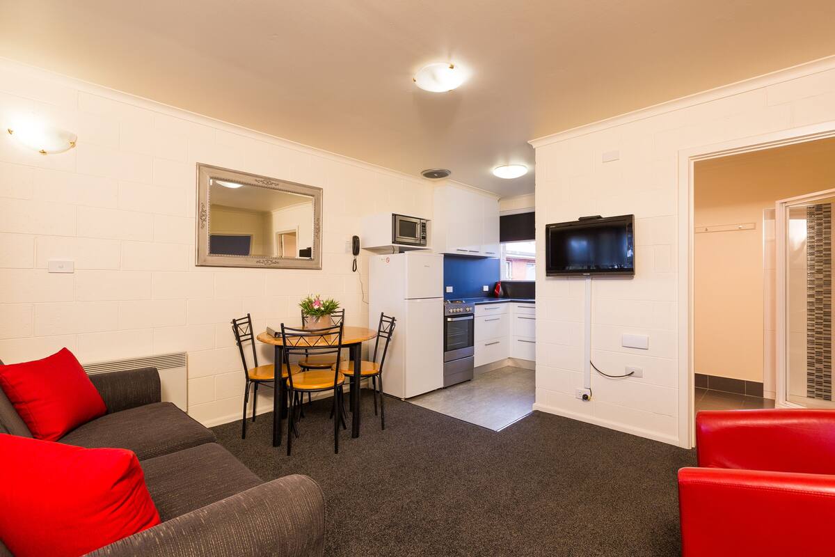 A compact living space with a kitchenette, a dining area with a table and chairs, and a sofa with red cushions.