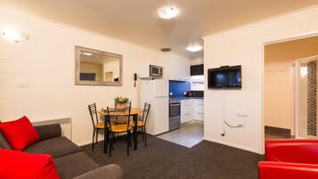 A compact living space with a kitchenette, a dining area with a table and chairs, and a sofa with red cushions.
