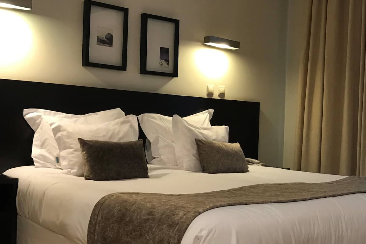 A neatly made bed with white linens and two pillows, a dark headboard, and two framed pictures on the wall.