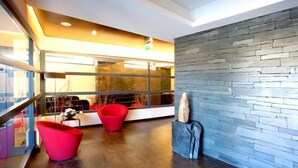 Un intérieur moderne avec un mur en pierre, deux chaises rouges et une statue.