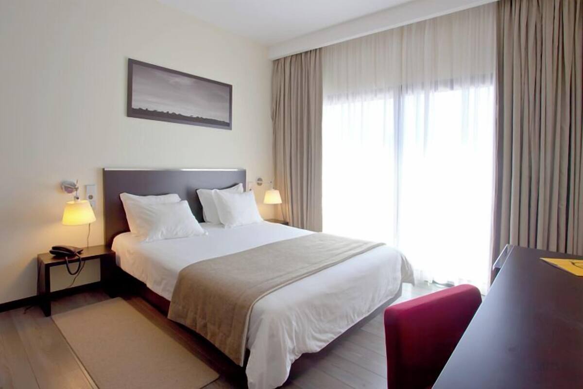 Una habitación de hotel con cama, lámparas de noche, un escritorio y una ventana con cortinas.