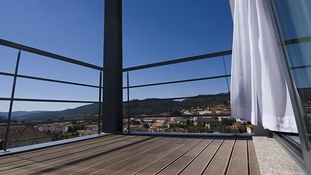 Un balcon doté d’un plancher en bois et de rampes en métal, offrant une vue sur une ville avec des maisons et des collines à l’horizon.