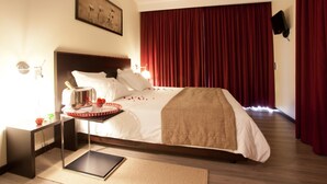Une chambre d’hôtel avec un grand lit, une table de chevet avec une lampe, une petite table avec un plateau, et un tableau au mur.
