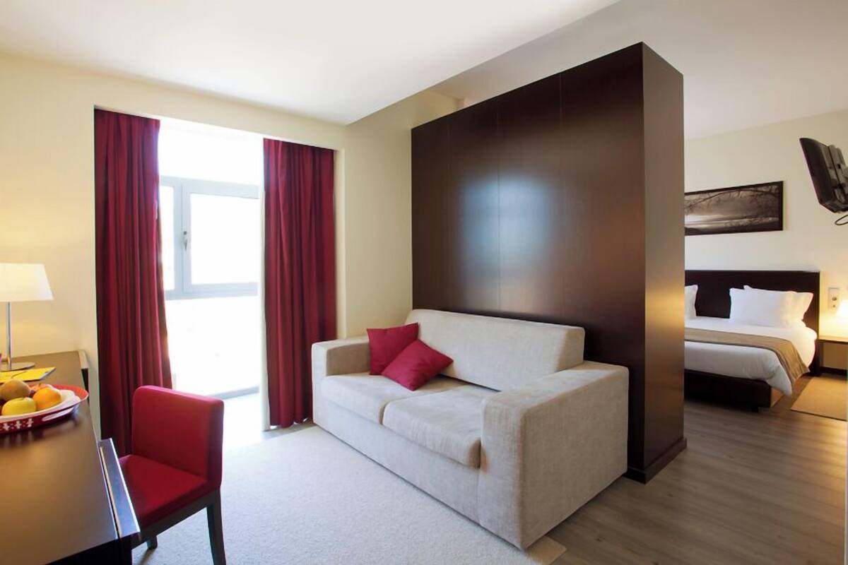 Habitación de hotel con sofá, una silla, una mesa de comedor con fruta, cama y un cuadro en la pared.