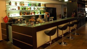 Un espace bar doté d’un long comptoir, de nombreux tabourets et d’une étagère bien garnie de diverses bouteilles.