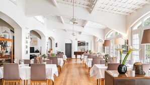 A spacious dining area with white tables and chairs, wooden flooring, and large windows. - Imani Country House (Évora)