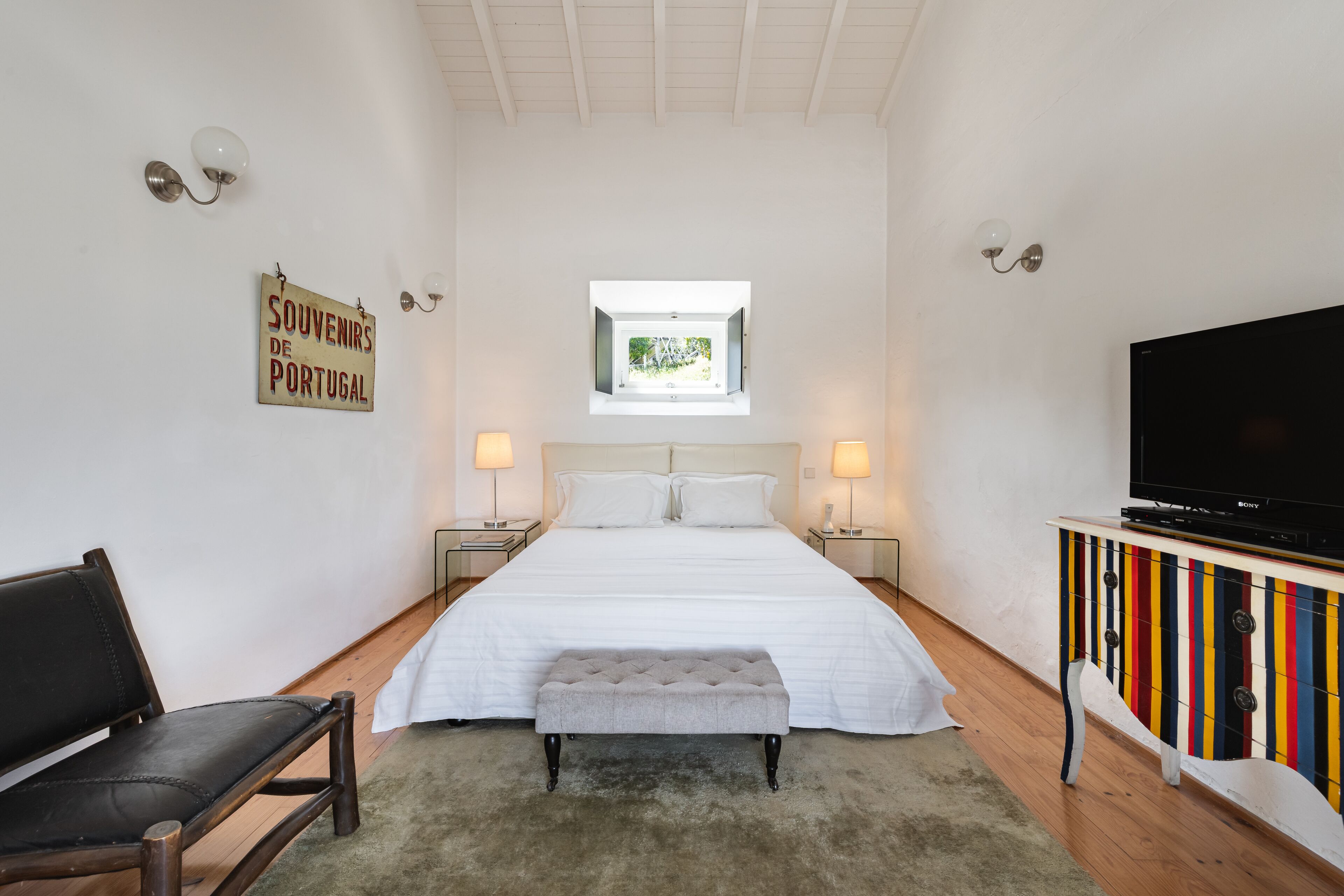 Un dormitorio con cama, un banco, un televisor y una ventana.