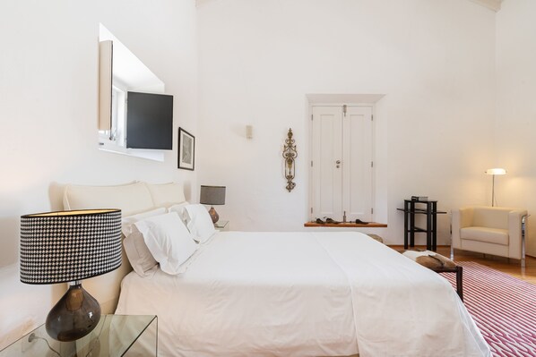 A bedroom with a bed, a bedside table with a lamp, a chair, and a door. - Imani Country House (Évora)