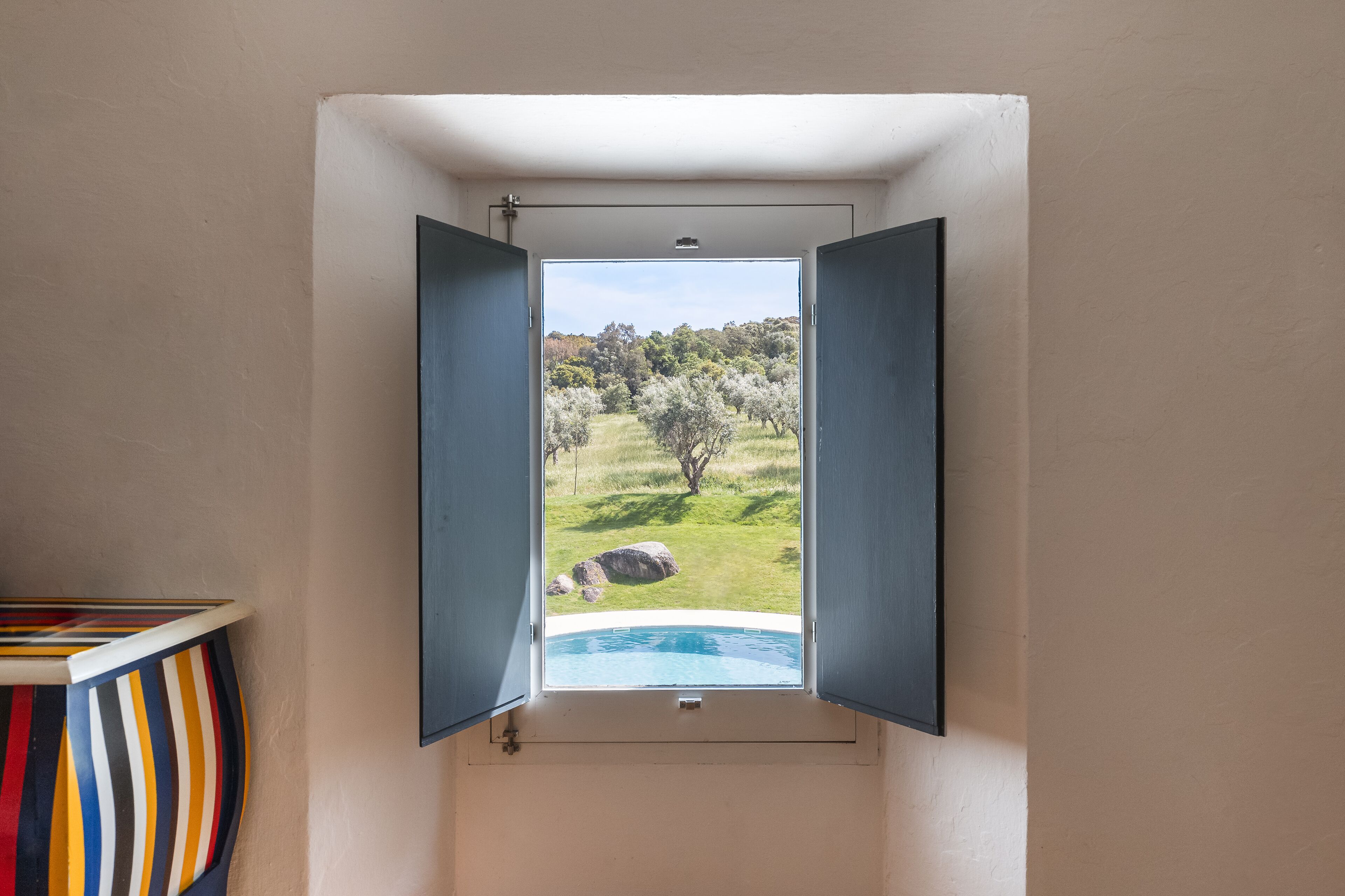 A room with a window overlooking a pool and a grassy landscape.
