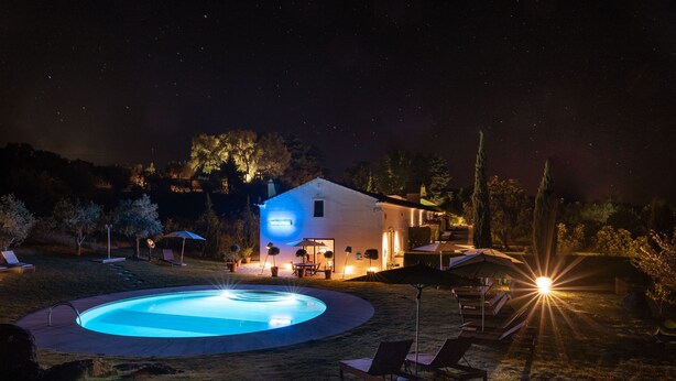 A nighttime scene with a swimming pool, lounge chairs, and a house with illuminated windows and a porch. - Imani Country House (Évora)