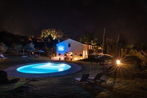 A nighttime scene with a swimming pool, lounge chairs, and a house with illuminated windows and a porch. - Imani Country House (Évora)