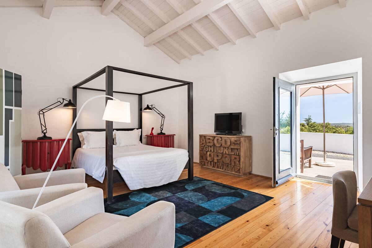 A bedroom with a four-poster bed, a television, a wooden cabinet with alphabet letters, and a view of the outdoors.