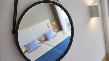 Espejo redondo que refleja una cama con ropa de cama azul y blanca, una mesita de noche y una lámpara de pared.