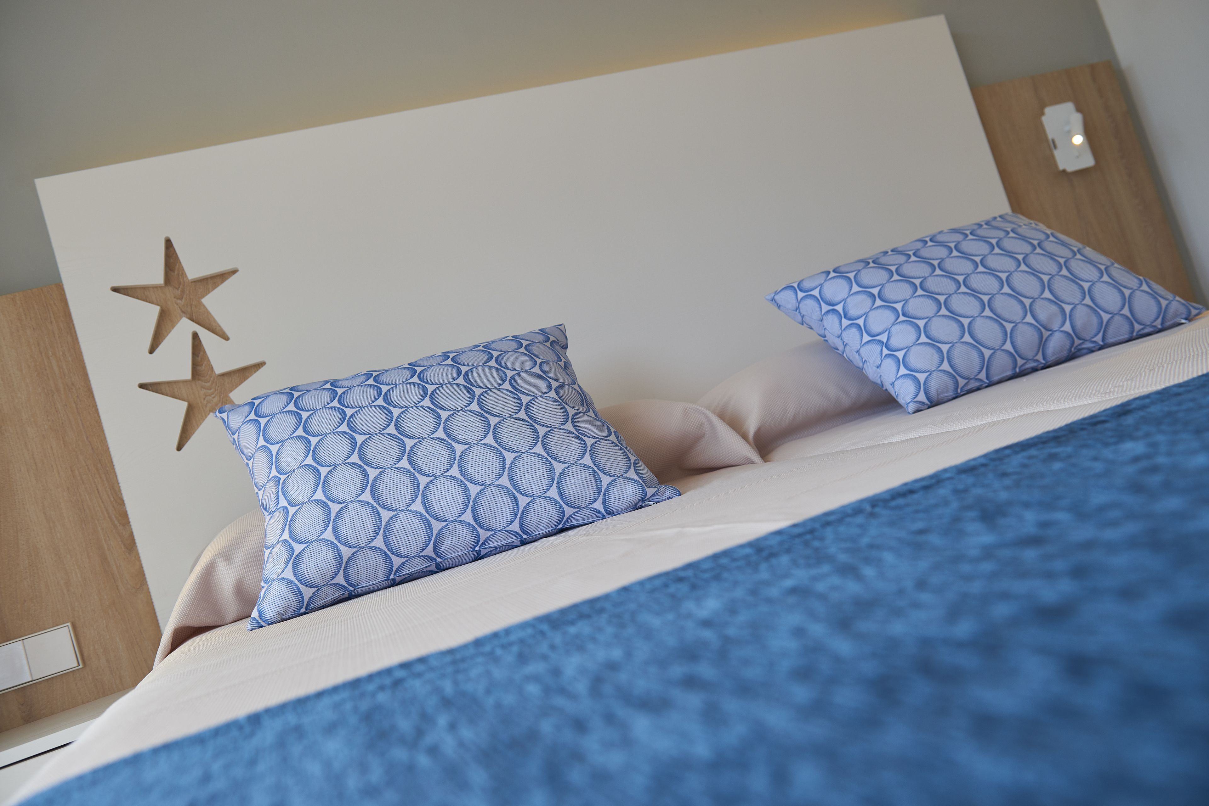 Een bed met twee gekleurde kussens, een houten hoofdbord en een blauwe deken.