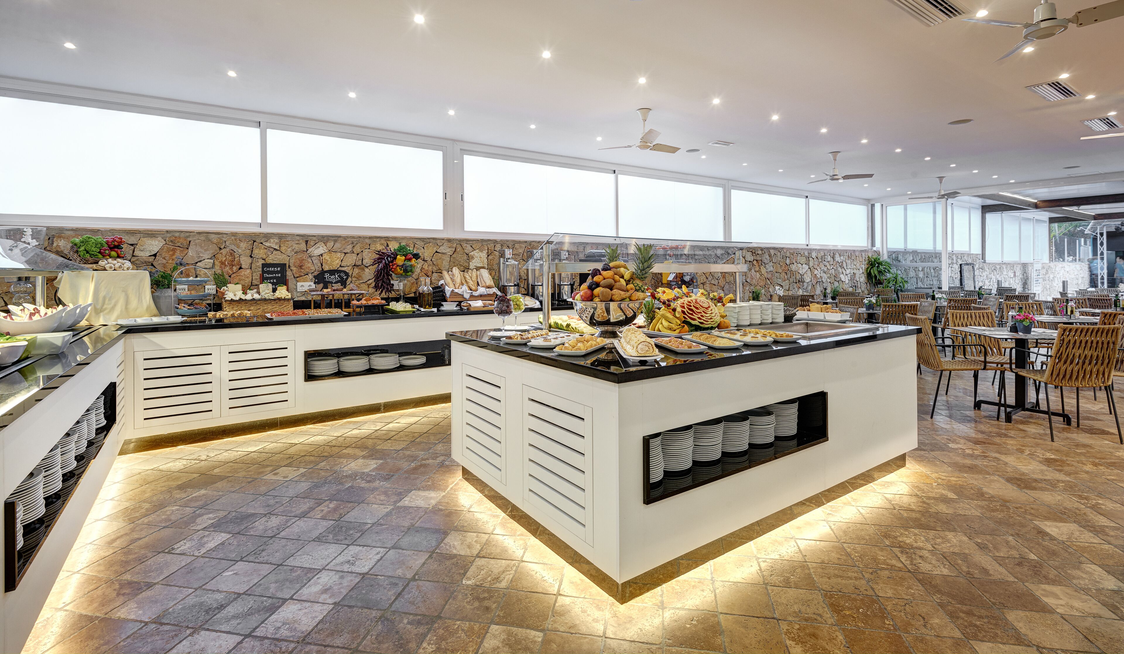 A buffet area with a variety of food items, a stone wall, and a seating area with tables and chairs.