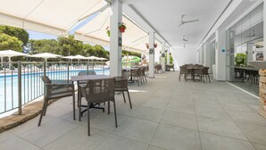 Un área de patio al aire libre con mesas y sillas, piscina y pared de vidrio.