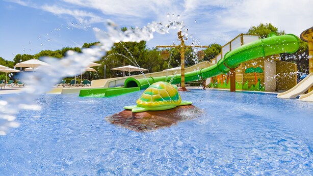 Un parque acuático con una piscina grande, toboganes y una fuente de agua con forma de tortuga.