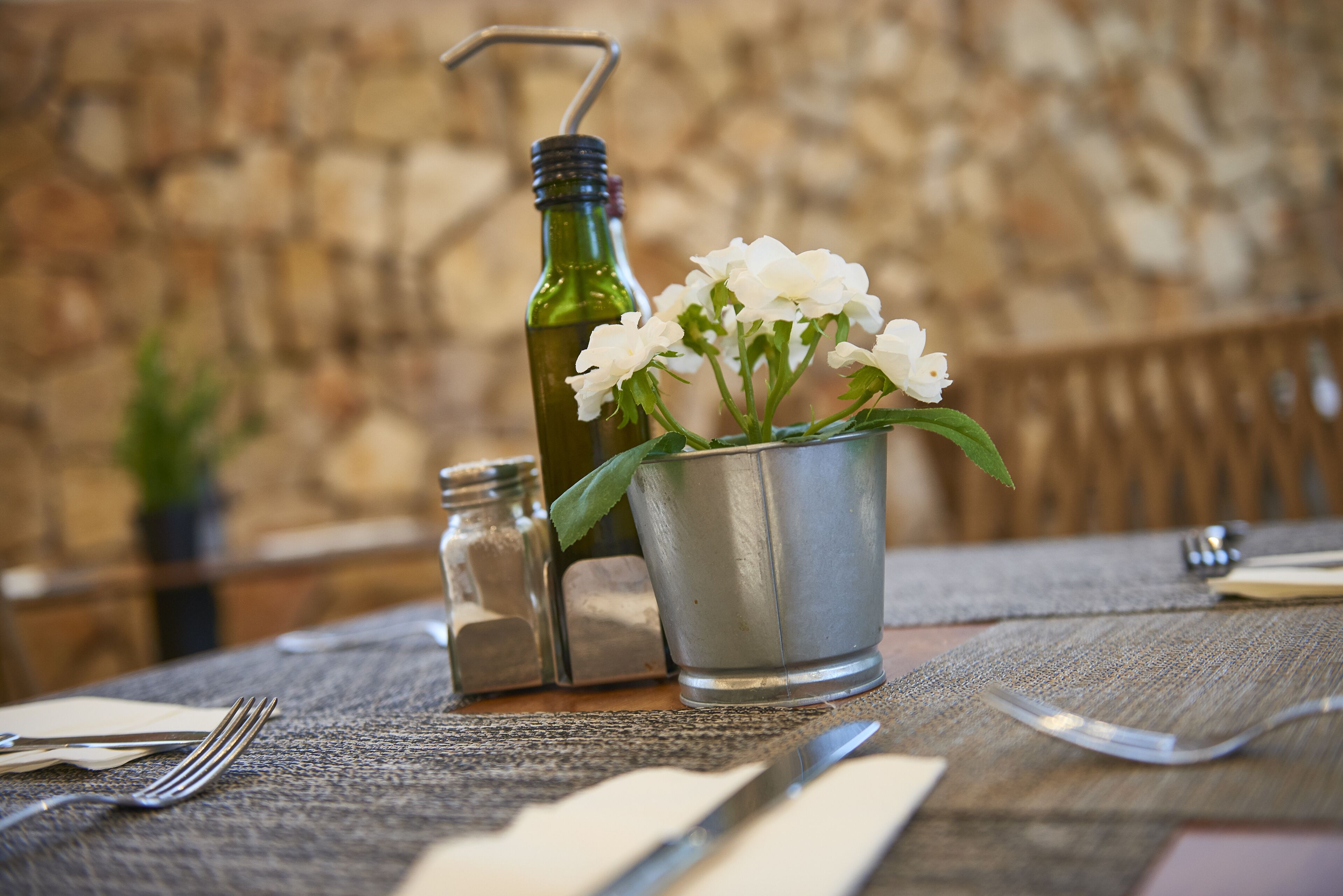 Een tafel gedekt met een metalen emmer gevuld met witte bloemen, een groene fles en zout- en peperstrooiers.