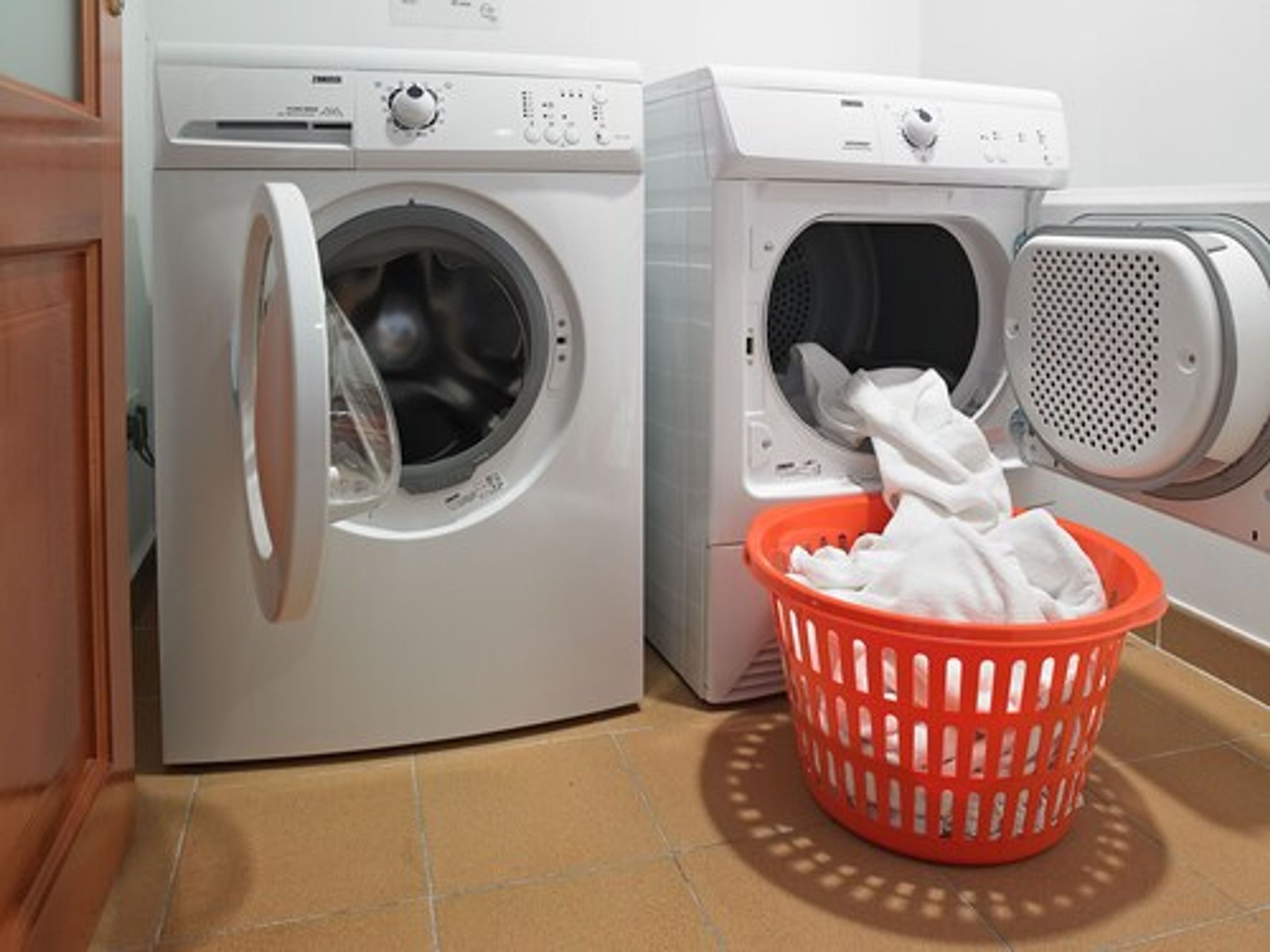 A laundry area with two front-loading washing machines and a red laundry basket filled with clothes.