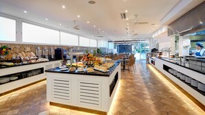 Montaje de bufé con diversos alimentos y una cocina al fondo.