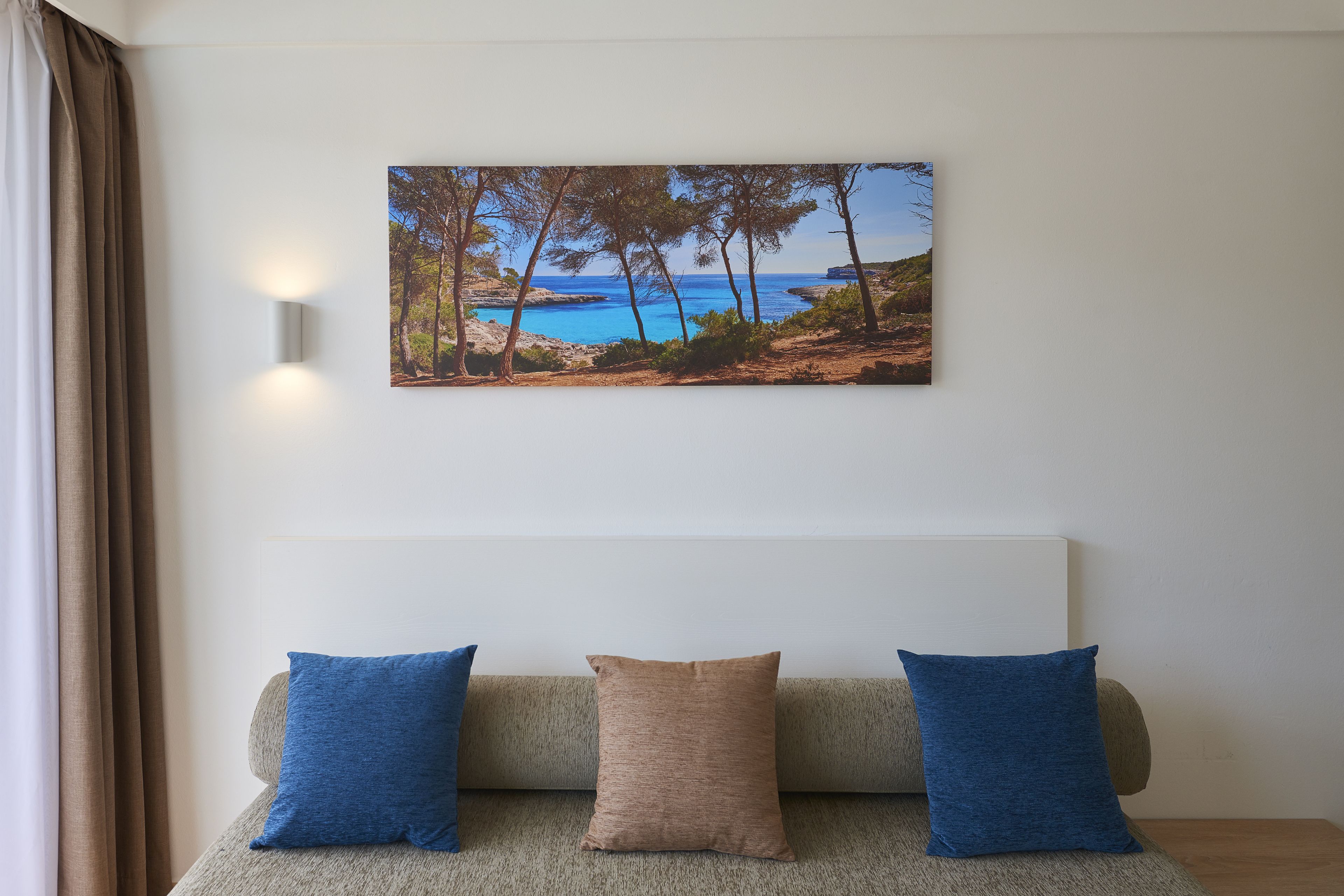 Una habitación con un sofá color beige, dos almohadas azules y un cuadro en el pared con un paisaje costero enmarcado.