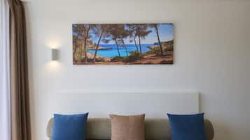 Una habitación con un sofá color beige, dos almohadas azules y un cuadro en el pared con un paisaje costero enmarcado.