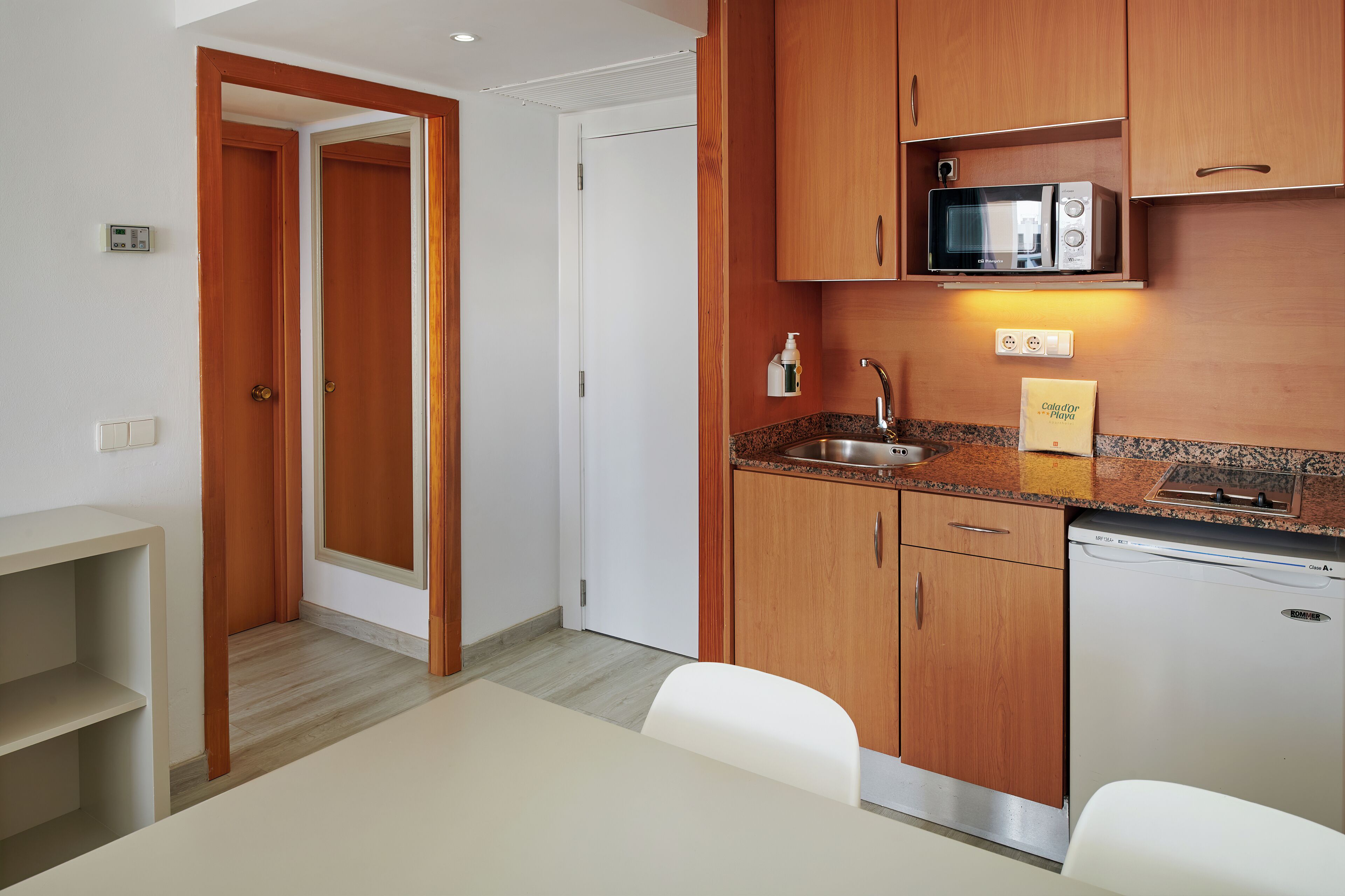 Una cocina compacta con armarios de madera, microondas, lavamanos y un refrigerador pequeño.