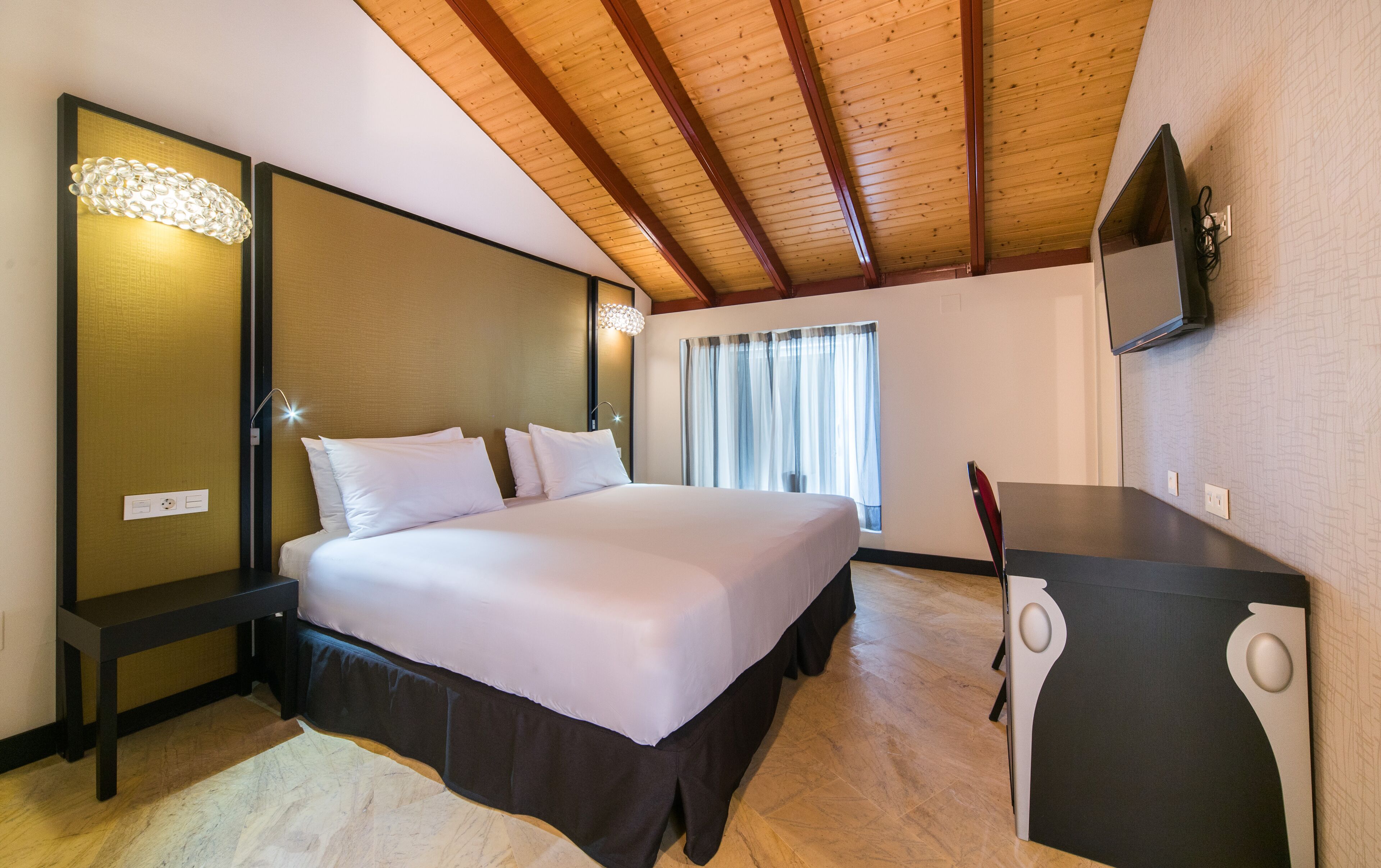 Un dormitorio con cama, escritorio, espejo y ventana con cortinas.