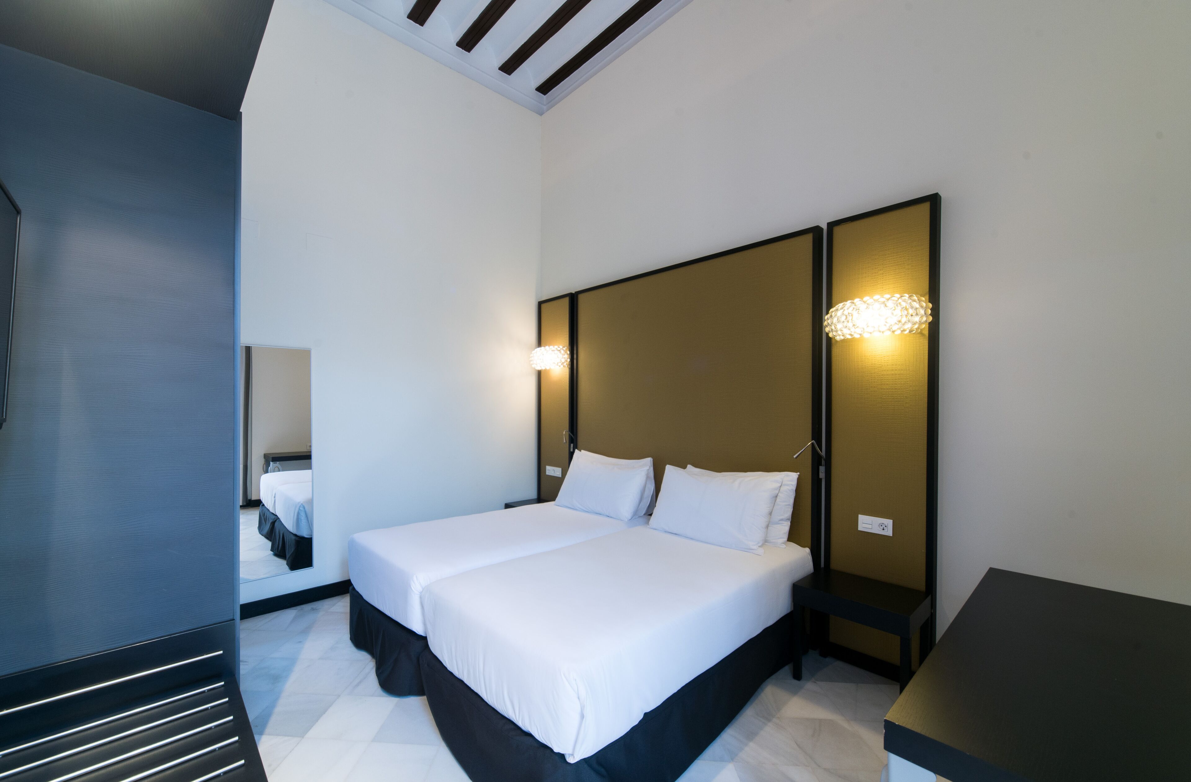 A modern hotel room with a large bed, bedside tables, and a mirror.