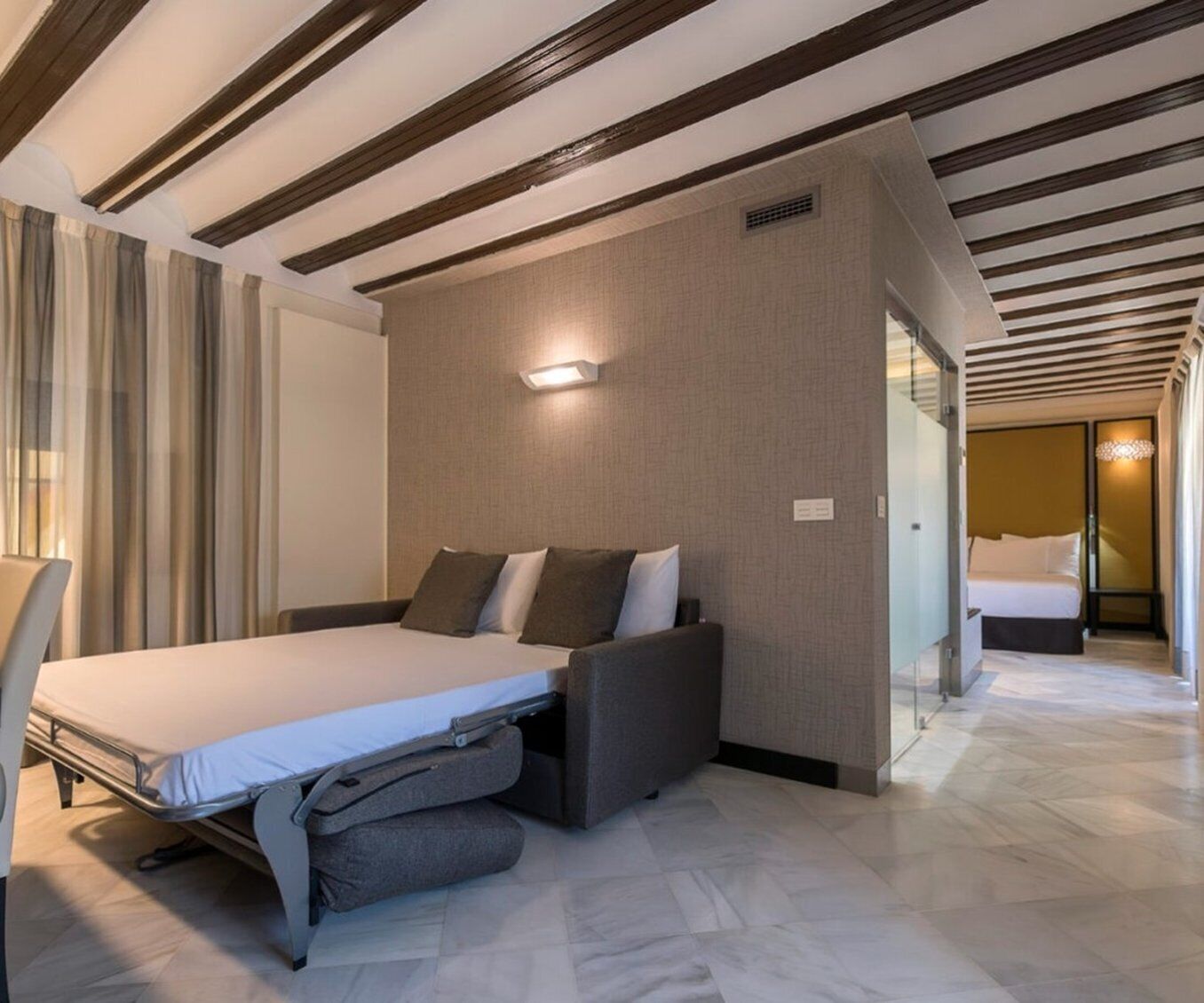 A modern hotel room with a bed, a seating area, and a separate sleeping area.