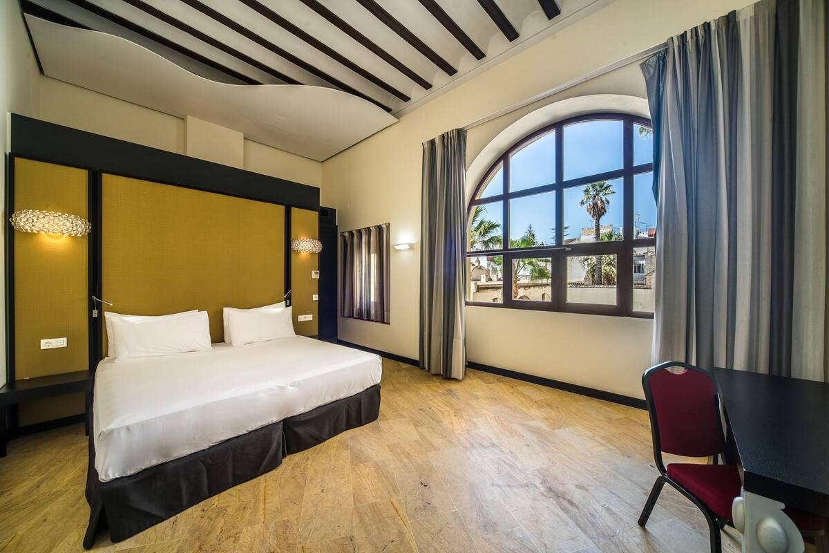 Habitación de hotel con una cama grande, un escritorio y una ventana con cortinas.