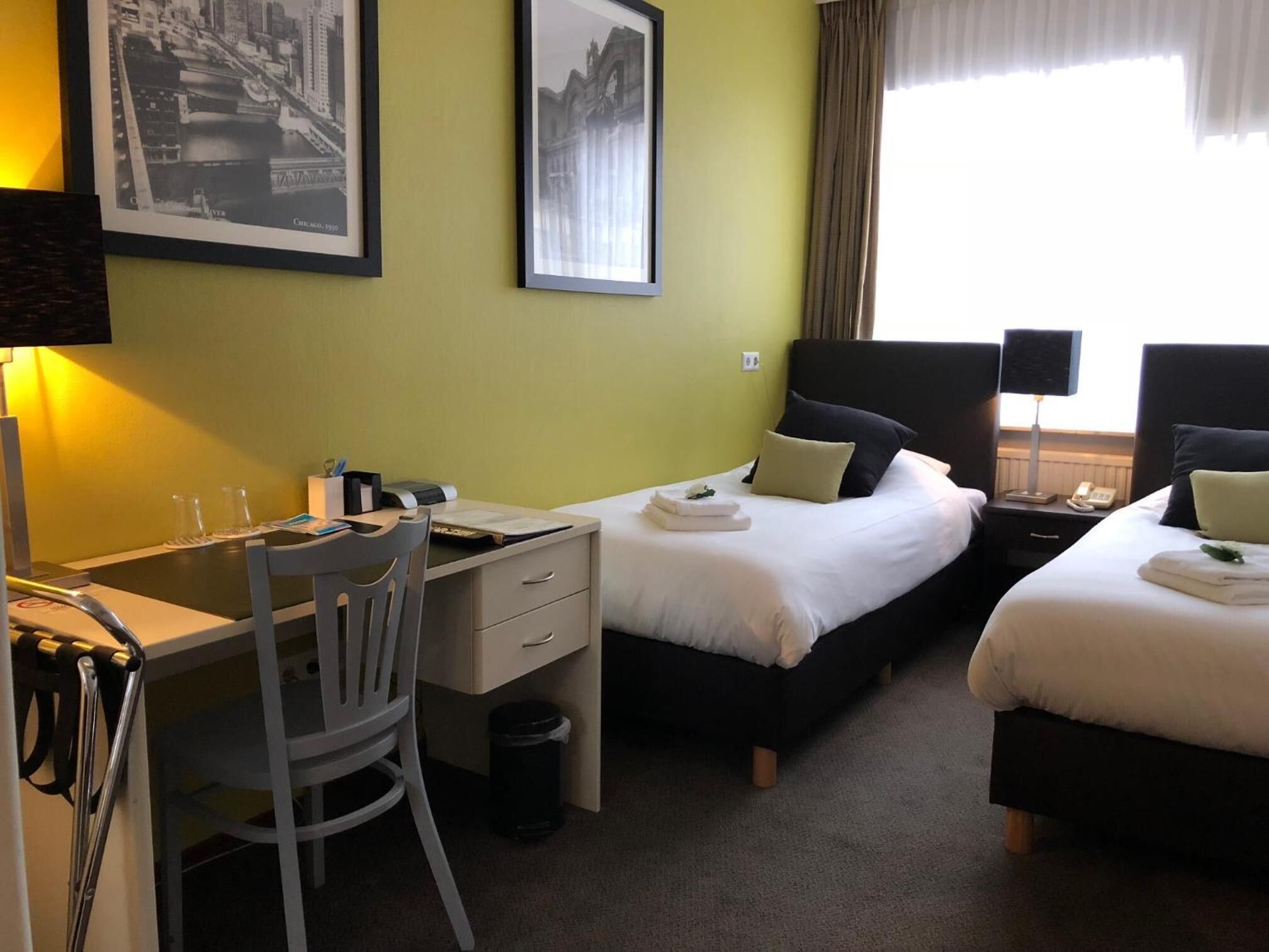 Ein Hotelzimmer mit Schreibtisch, zwei Betten, einem Sessel und einem Mülleimer.