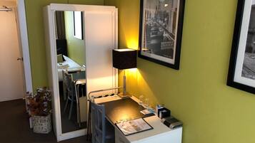 Habitación de hotel con cama, escritorio con silla, espejo, lámpara y un cuadro en la pared.
