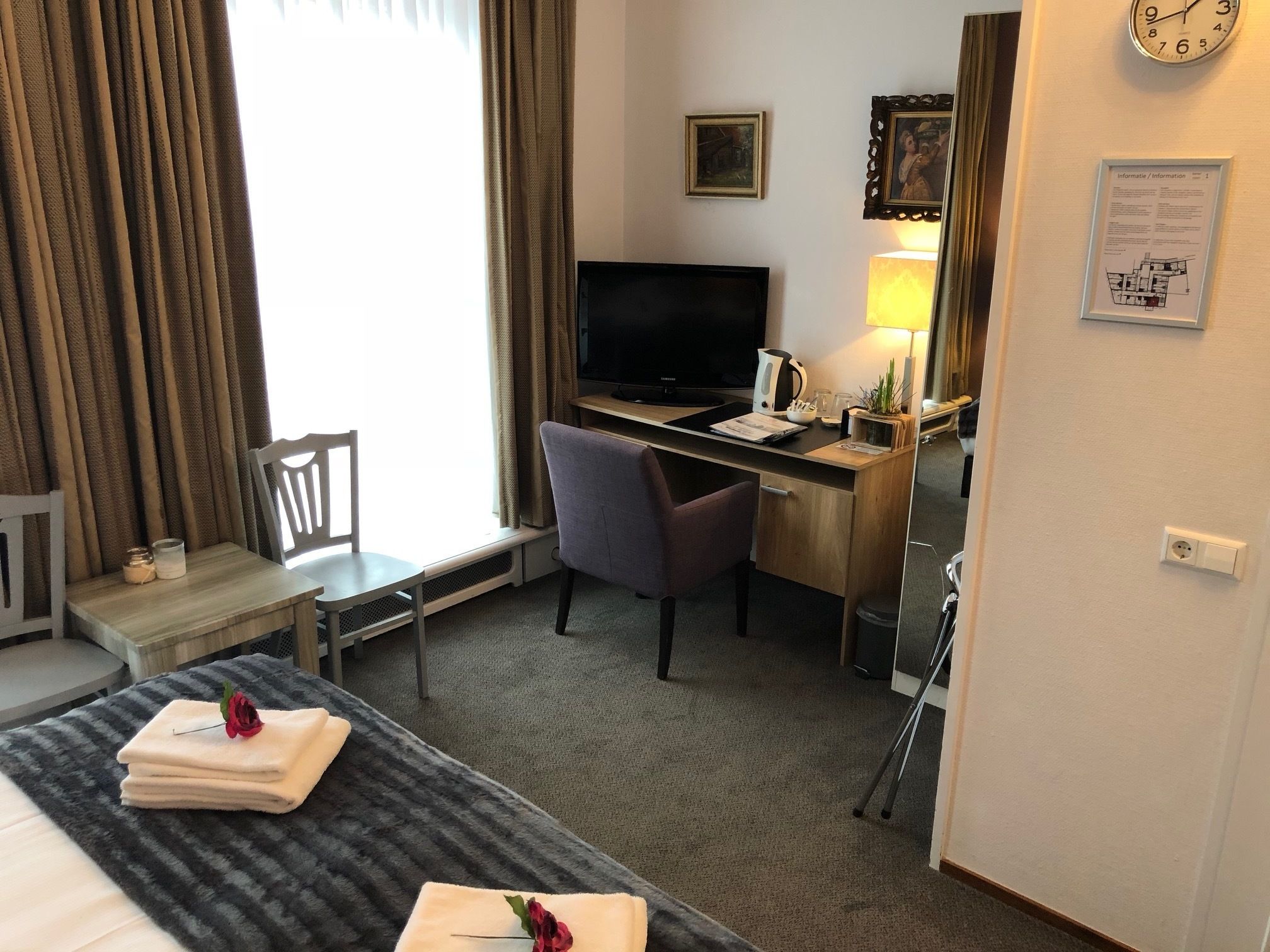 Una camera d'hotel con un letto, una scrivania con un computer, una sedia, una televisione e una lampada.