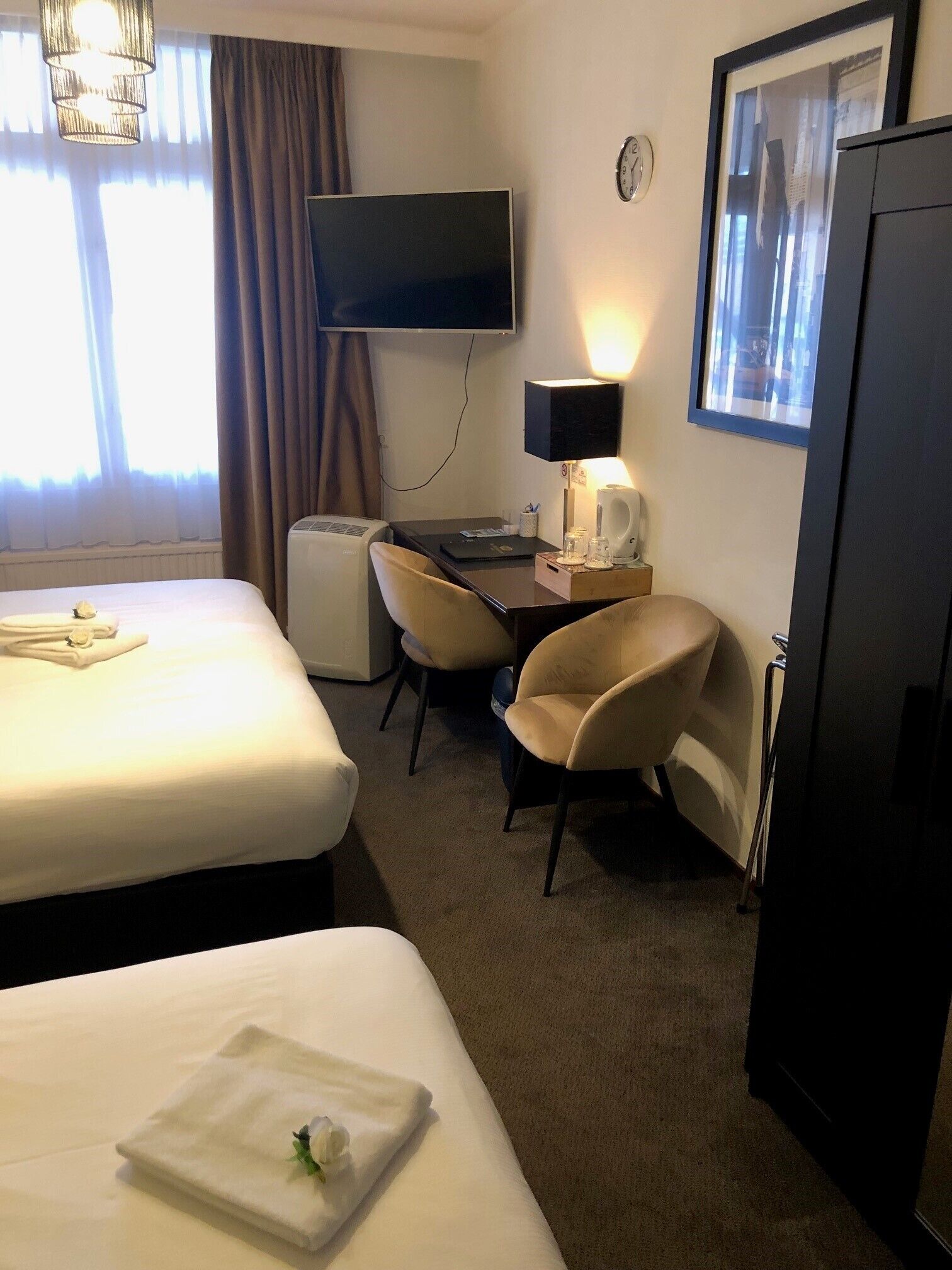 Habitación de hotel con dos camas, un escritorio con silla, un televisor de pantalla plana, un reloj y un refrigerador.
