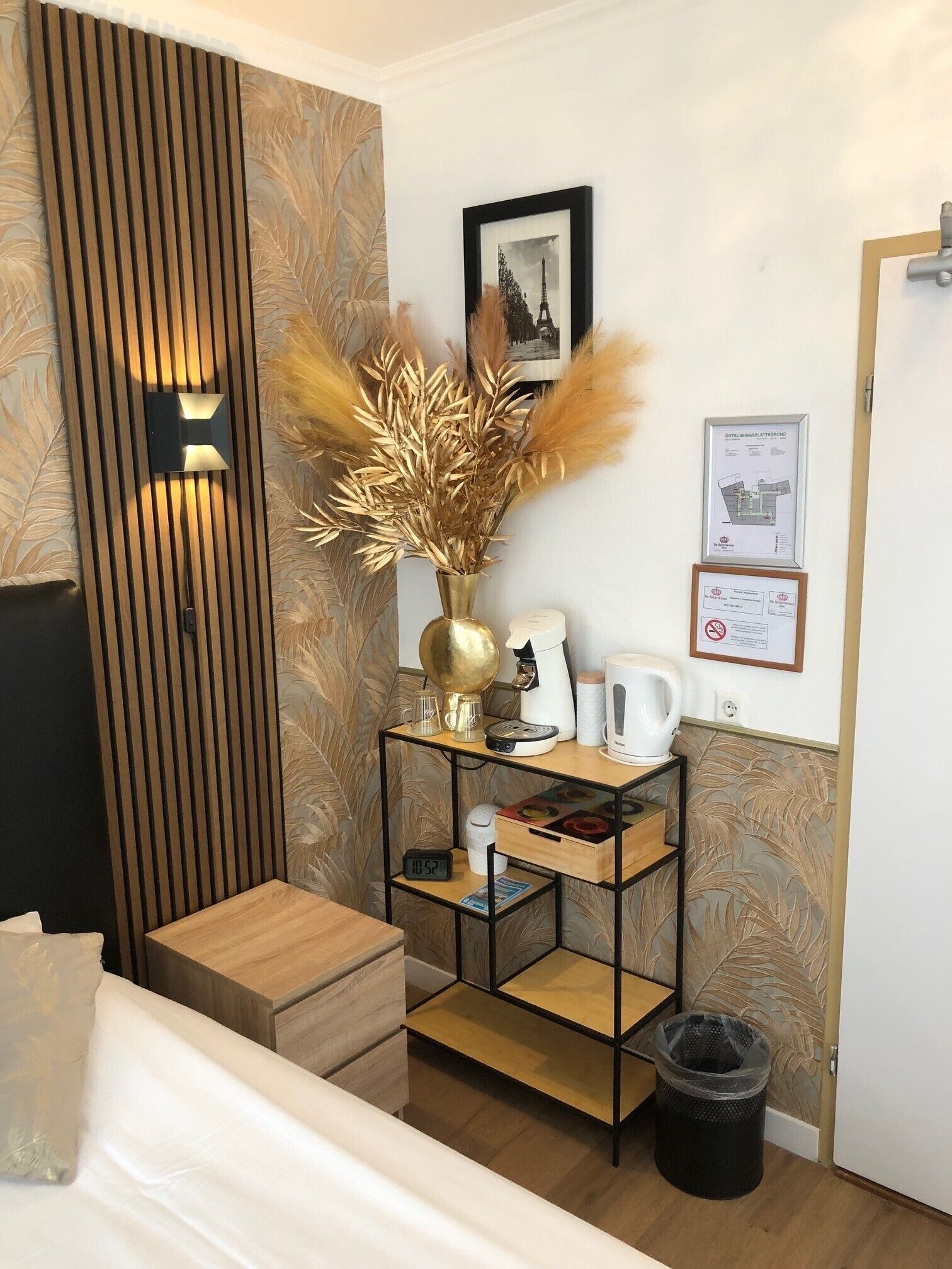 A hotel room with a wooden panel wall, a small wooden table with a vase of pampas grass, a framed picture of the Eiffel Tower, and a framed certificate on the wall.