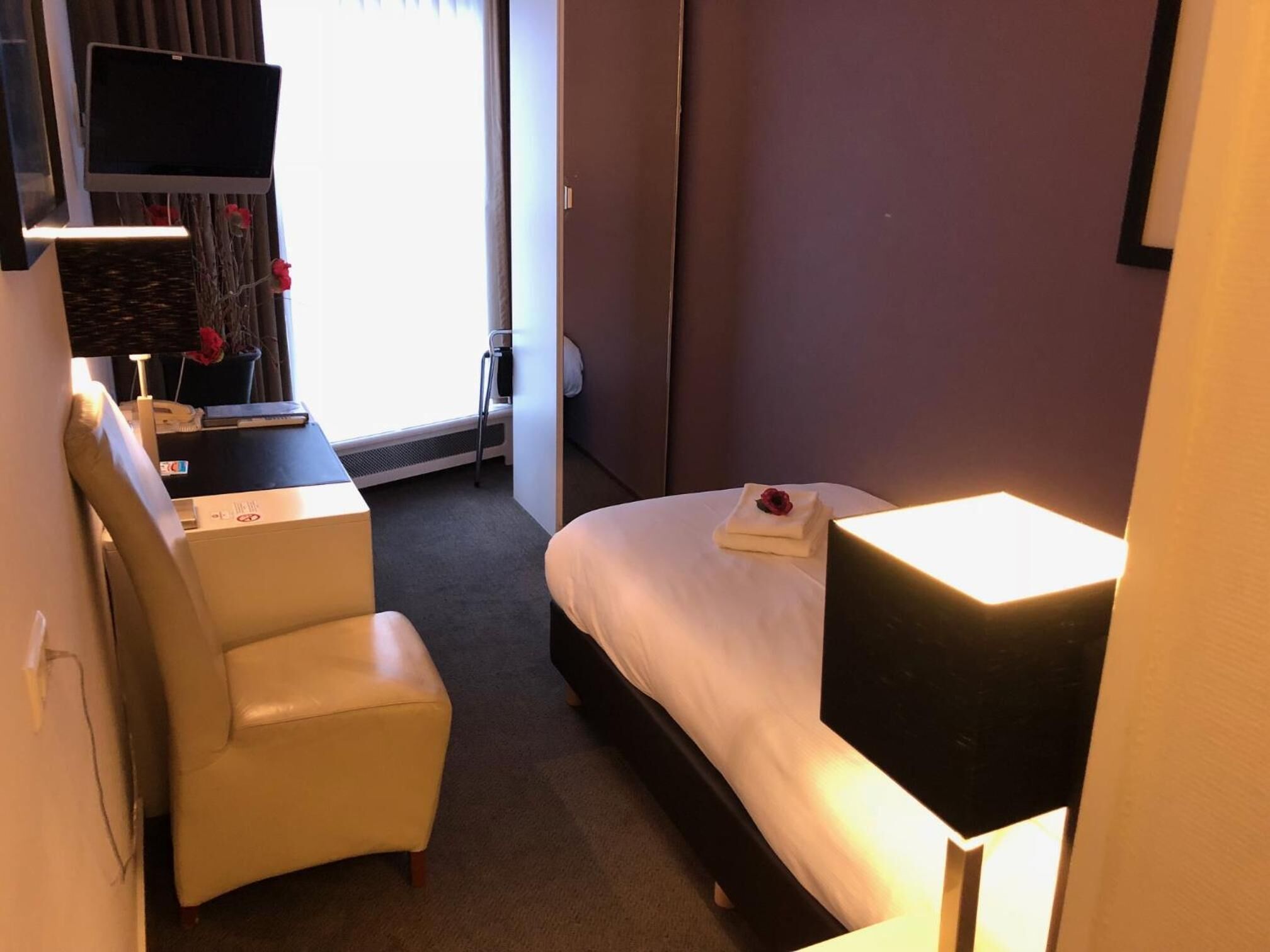 A hotel room with a bed, a desk, a chair, a TV, and a window with curtains.