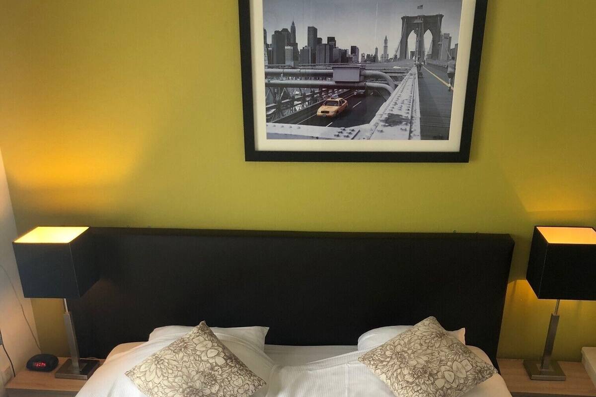 Een hotelkamer met een bed, twee kussens, een ingelijst foto aan de muur en twee bedlampen.