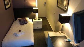 Una habitación de hotel con cama, mesita de noche, lámpara y escritorio con silla.