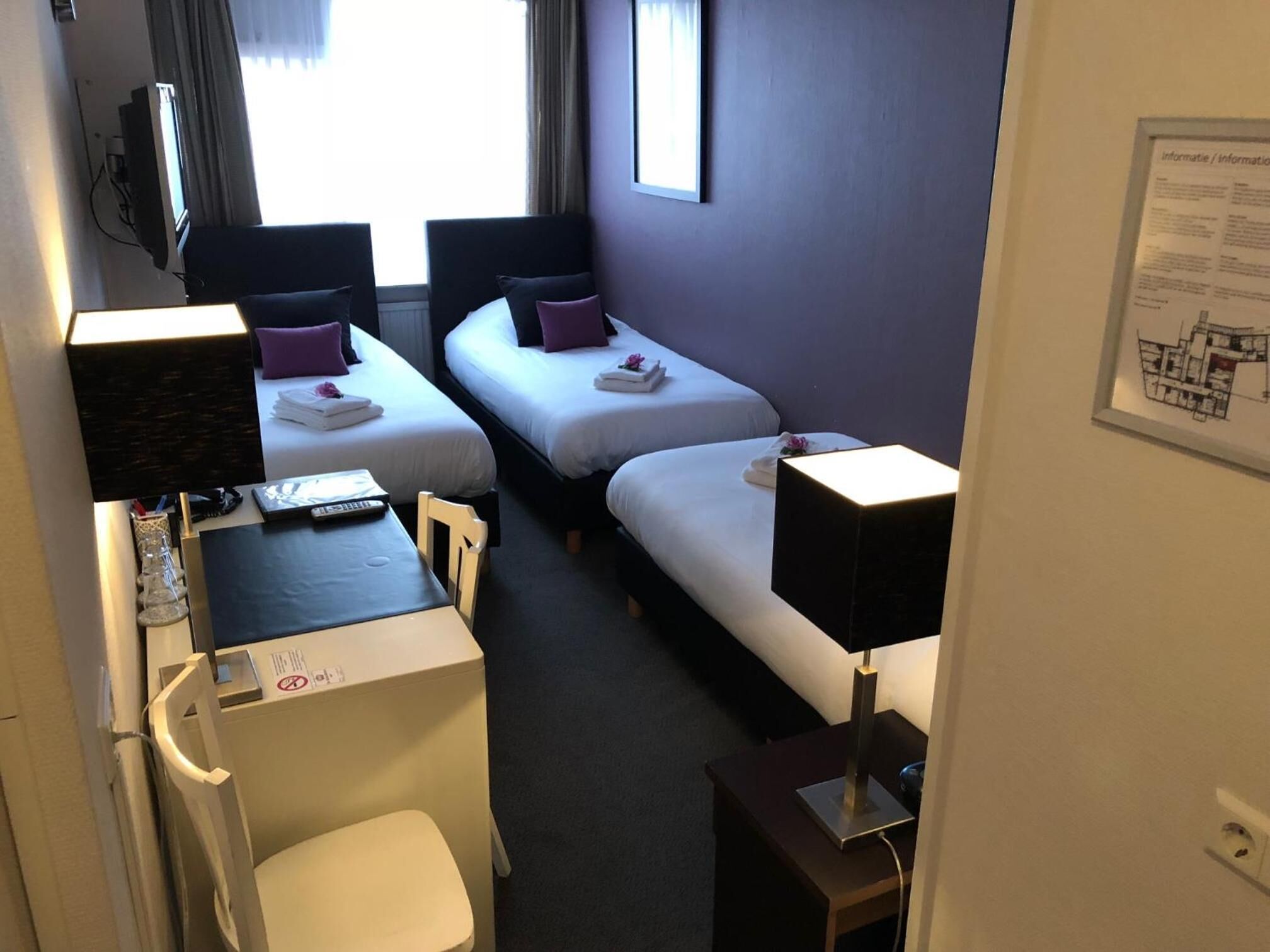 A compact hotel room with two single beds, a desk with a chair, a TV, and a small table.