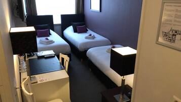 A compact hotel room with two single beds, a desk with a chair, a TV, and a small table.